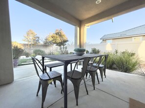 A covered patio with a table and chairs, a potted plant, and a view of the backyard. - Former Model Home, 3 Car Garage, Gym, Sleep 14 (Lancaster)