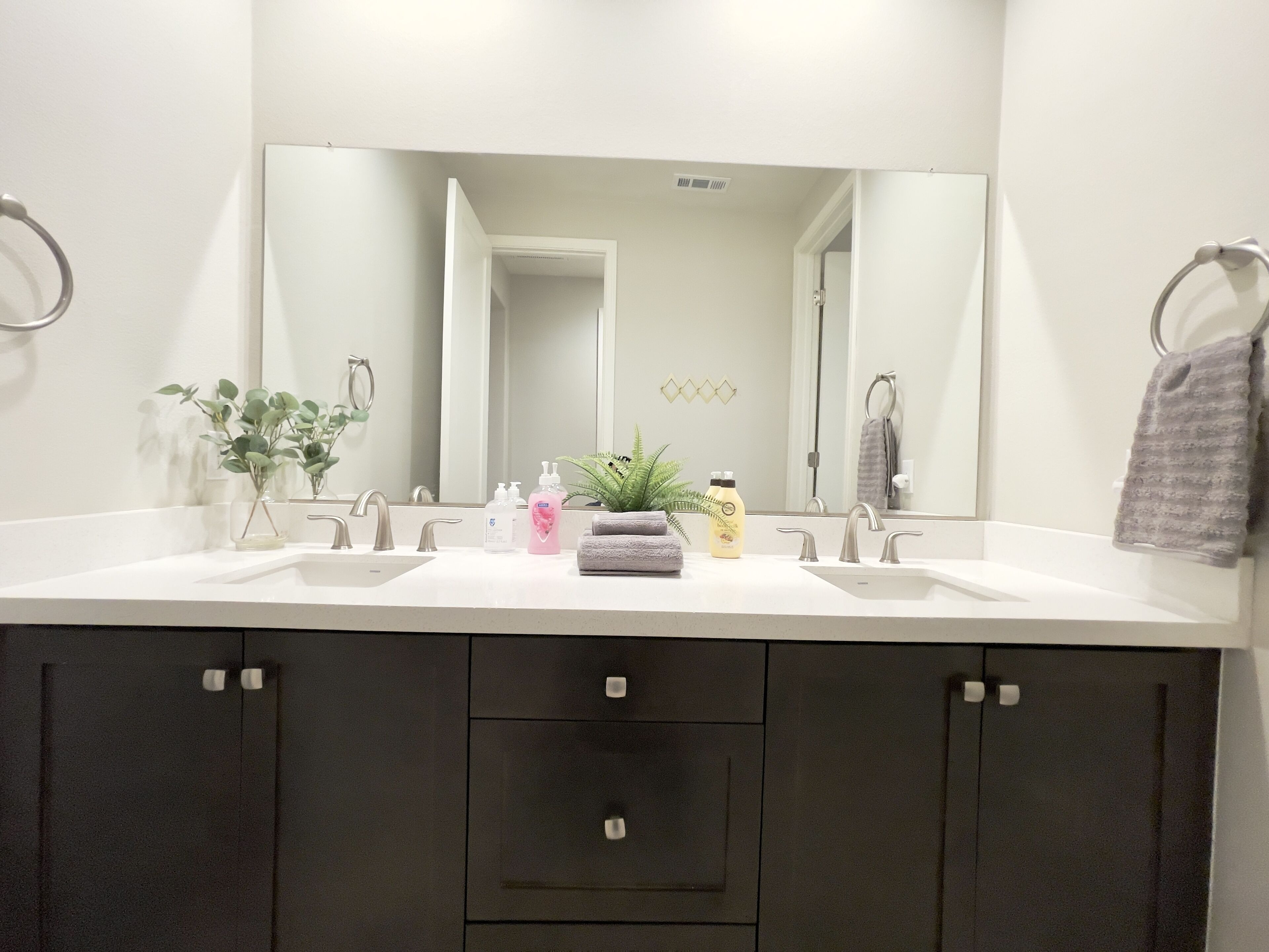 Un baño moderno con dos lavamanos, un espejo grande y armarios oscuros.