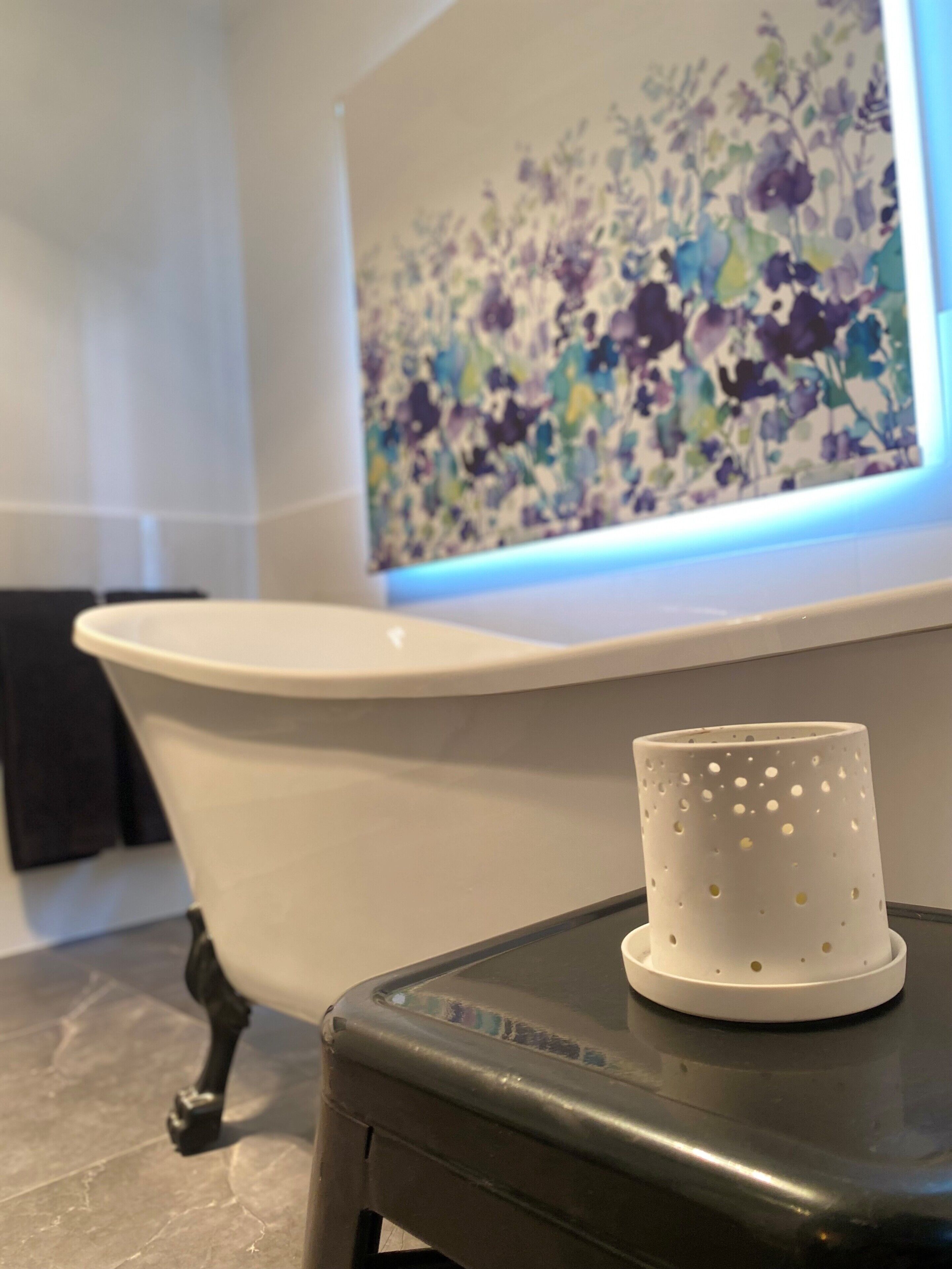 A bathroom with a white bathtub, a floral artwork on the wall, and a small stool with a white object on it.