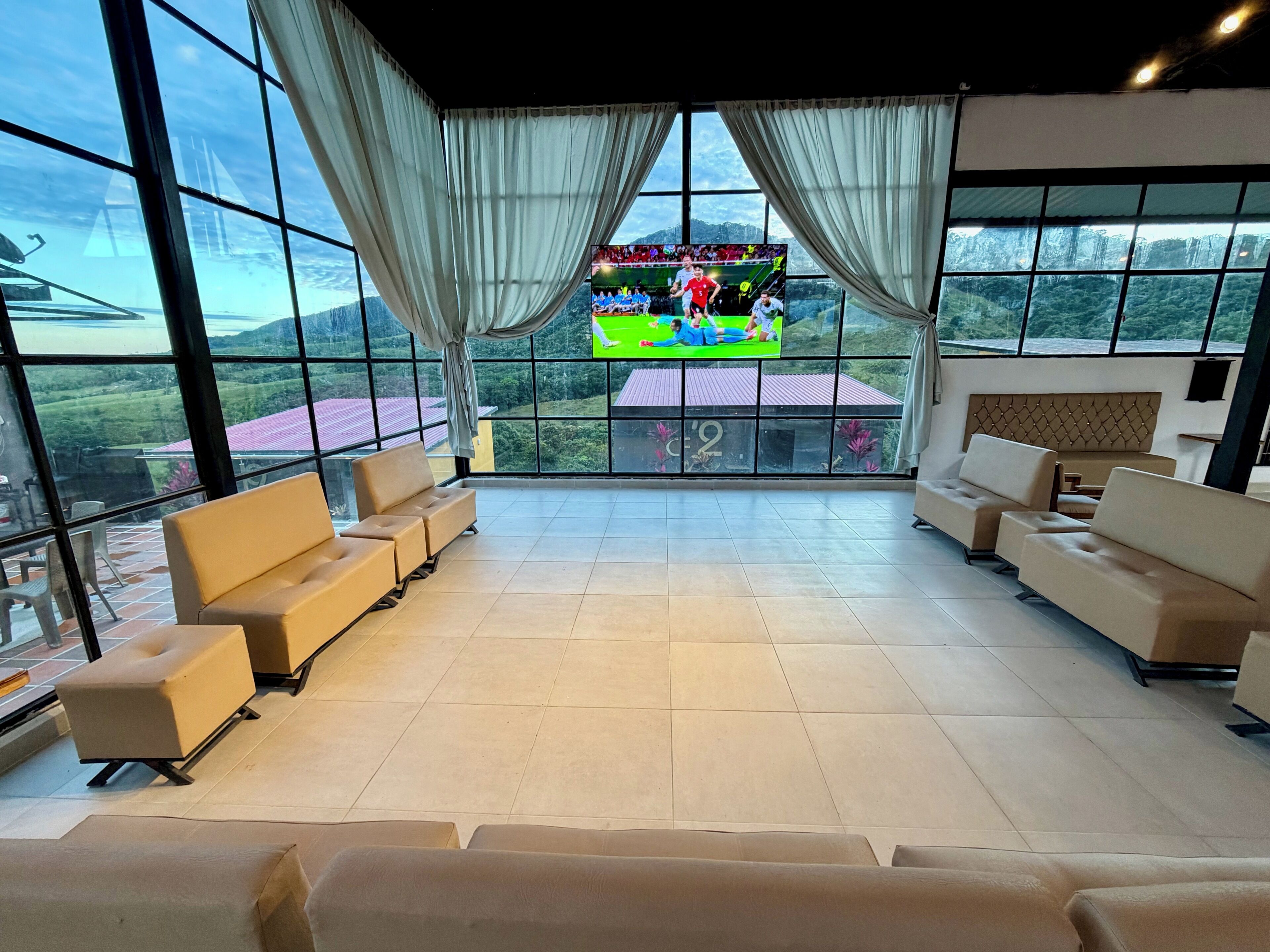 A spacious room with large windows, a flat-screen TV, and multiple seating areas.