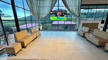 A spacious room with large windows, a flat-screen TV, and multiple seating areas.