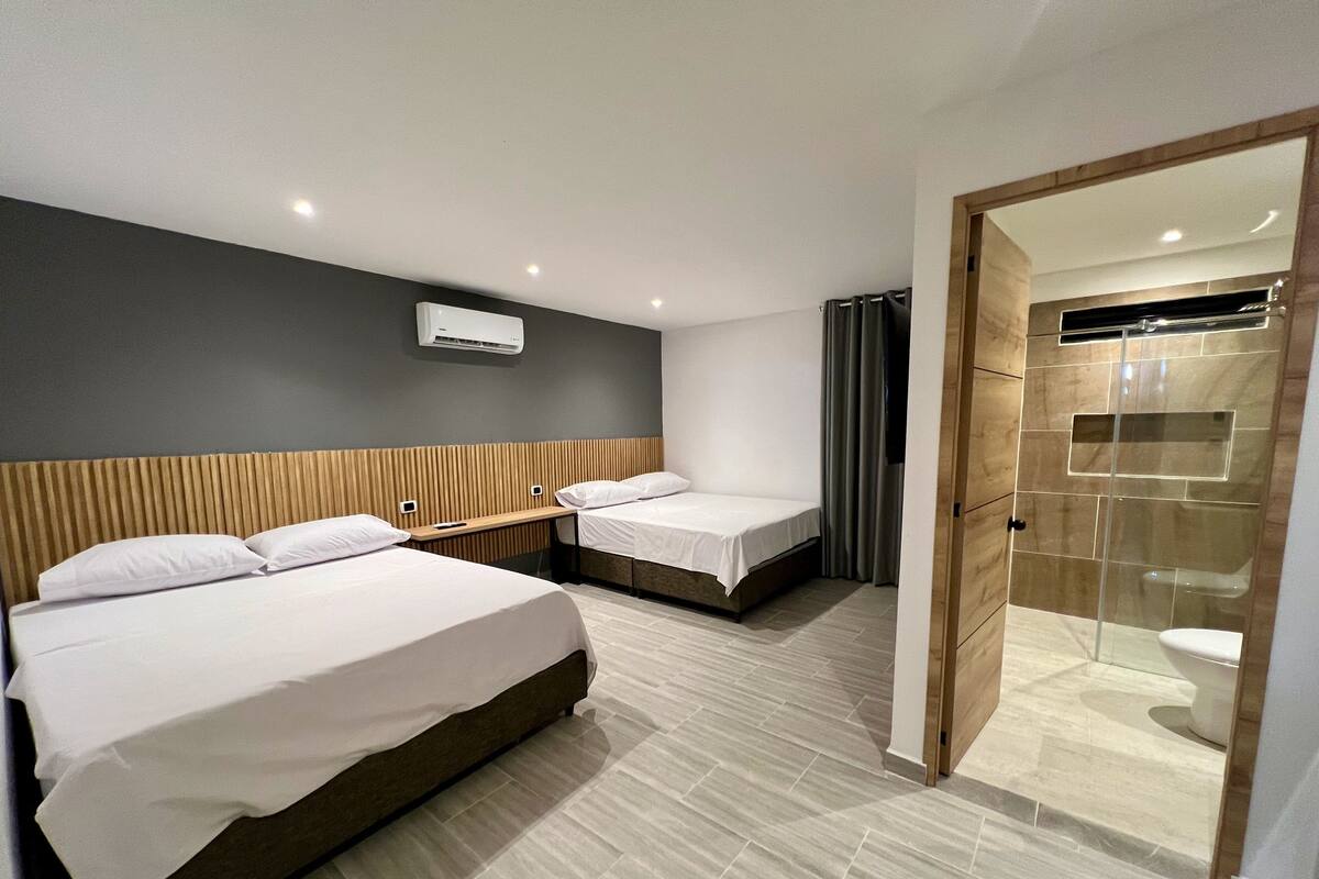 A modern hotel room with two beds, a shower area, and a mounted air conditioner.