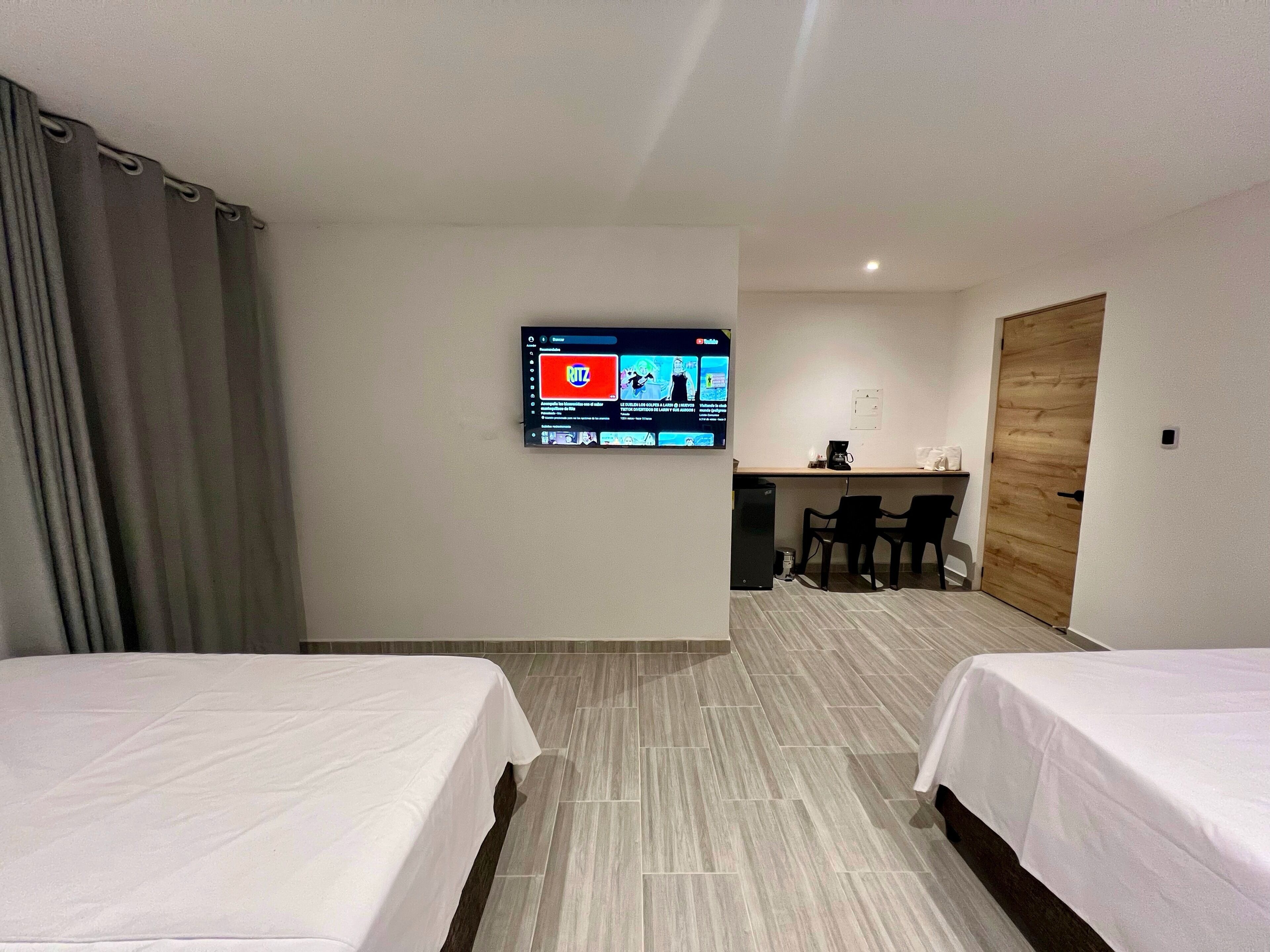 A hotel room with two beds, a desk, a chair, a television mounted on the wall, and a wooden door.