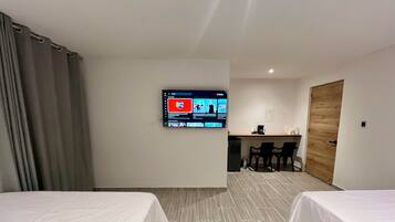 A hotel room with two beds, a desk, a chair, a television mounted on the wall, and a wooden door.