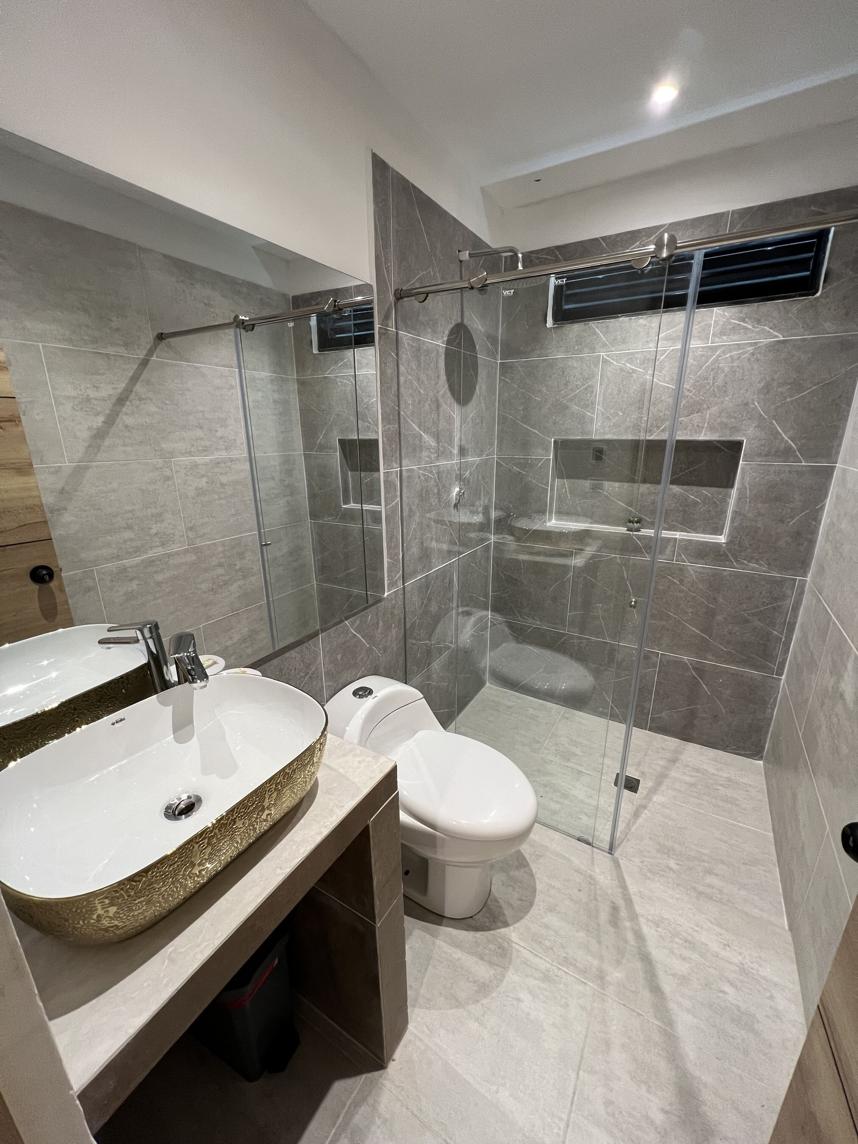 Une salle de bain moderne avec deux lavabos, des toilettes et une douche séparée par une paroi de verre.