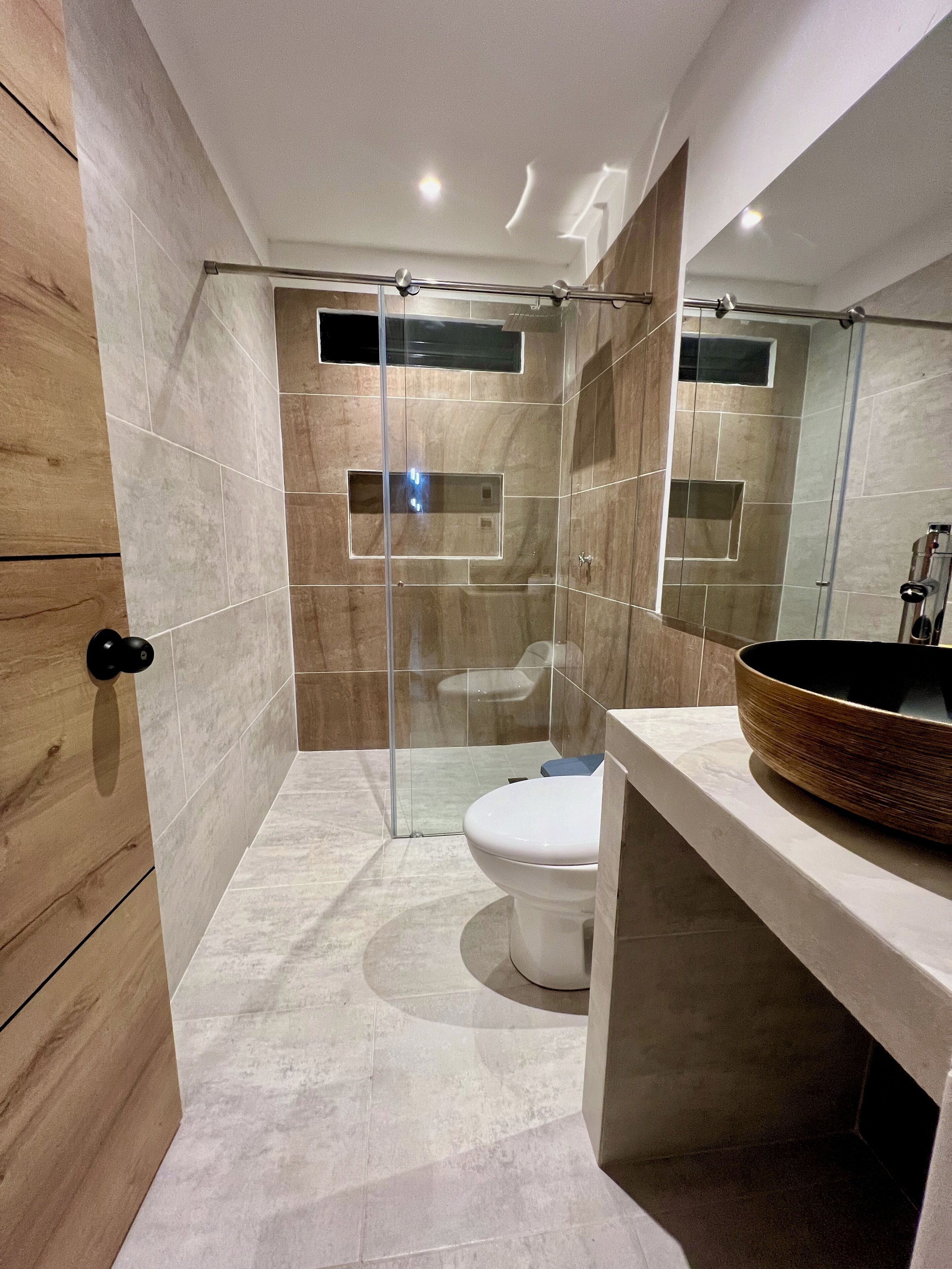 Une salle de bain moderne dotée d’une douche à parois de verre, de toilettes et d’un meuble-lavabo avec un grand lavabo en cuve.