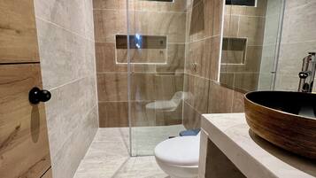 Une salle de bain moderne dotée d’une douche à parois de verre, de toilettes et d’un meuble-lavabo avec un grand lavabo en cuve.