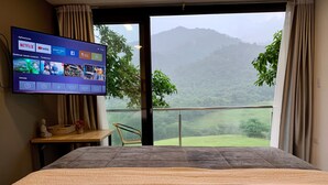 Habitación de hotel con una cama grande, un televisor en la pared y un balcón con vistas a las montañas.