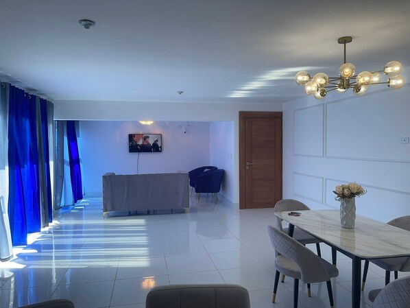 A modern living room with a dining area, a TV mounted on the wall, and a wooden door.