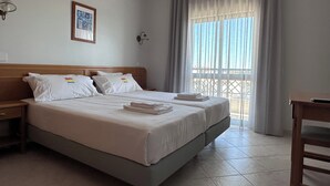 Quarto de hotel com cama, duas mesas de cabeceira, janela com cortinas e vista exterior.