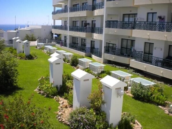 A modern hotel with multiple balconies, a well-maintained garden, and a clear view of the sea.