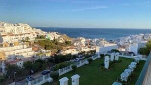 Uma área residencial costeira com edifícios brancos, um pátio ajardinado e vista para o mar.