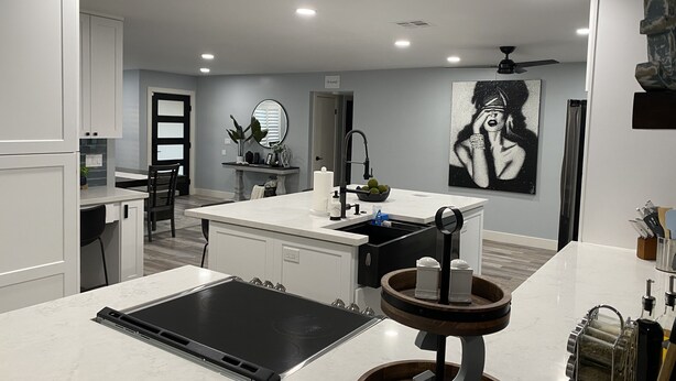 A modern kitchen with white cabinetry, a black induction cooktop, and a wooden serving tray.