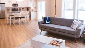 En moderne stue med sofa, sofabord og et spiseområde med stole og bord.