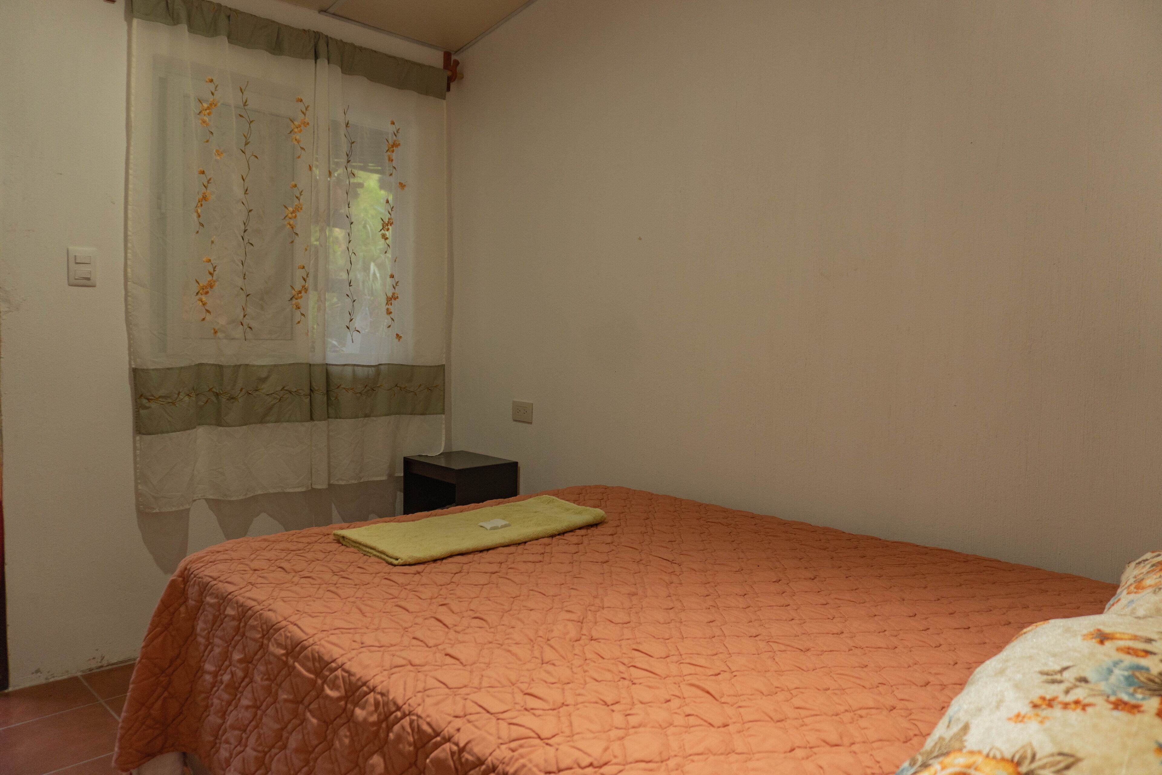 Une chambre avec un lit simple, une table de chevet et une fenêtre ornée de rideaux légers.