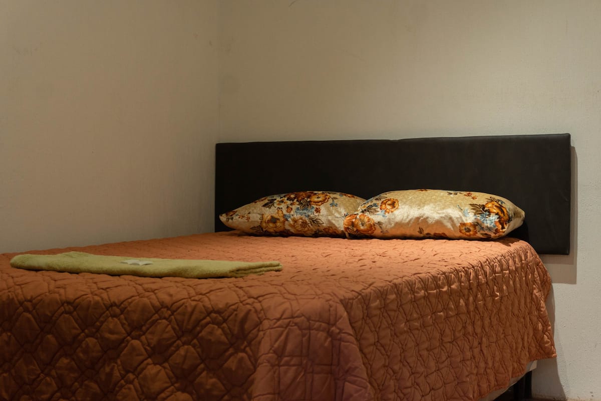 Ein Bett mit einer gesteppten braunen Decke, zwei blumigen Kissen und einer grünen Decke.