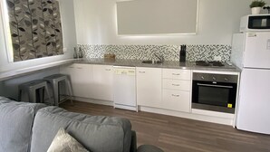 Uma cozinha moderna com armários brancos, micro-ondas e forno. Há um ventilador de teto, um sofá cinza com almofada decorativa e um painel de parede decorativo.
