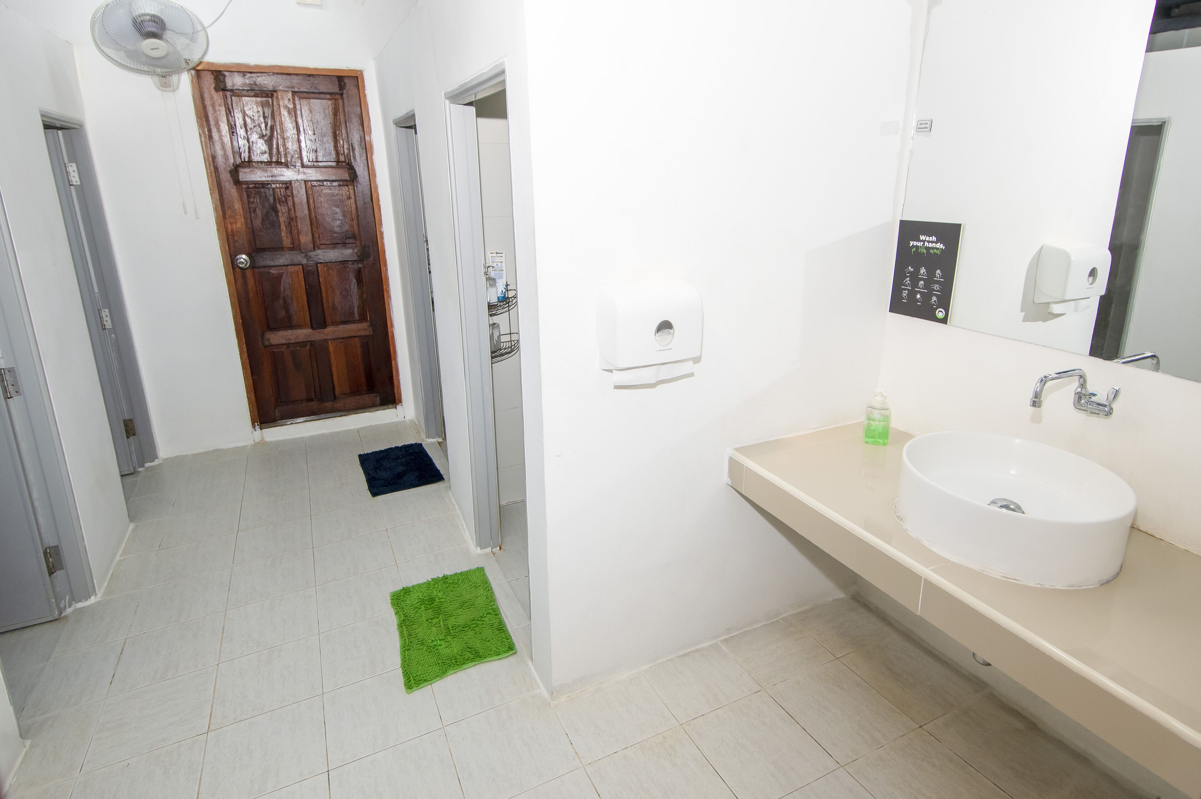 Een badkamer met een witte wastafel, een spiegel, een zeepdispenser en een houten deur.