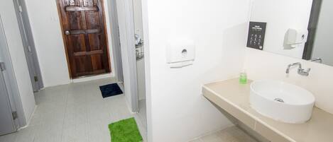 Een badkamer met een witte wastafel, een spiegel, een zeepdispenser en een houten deur.