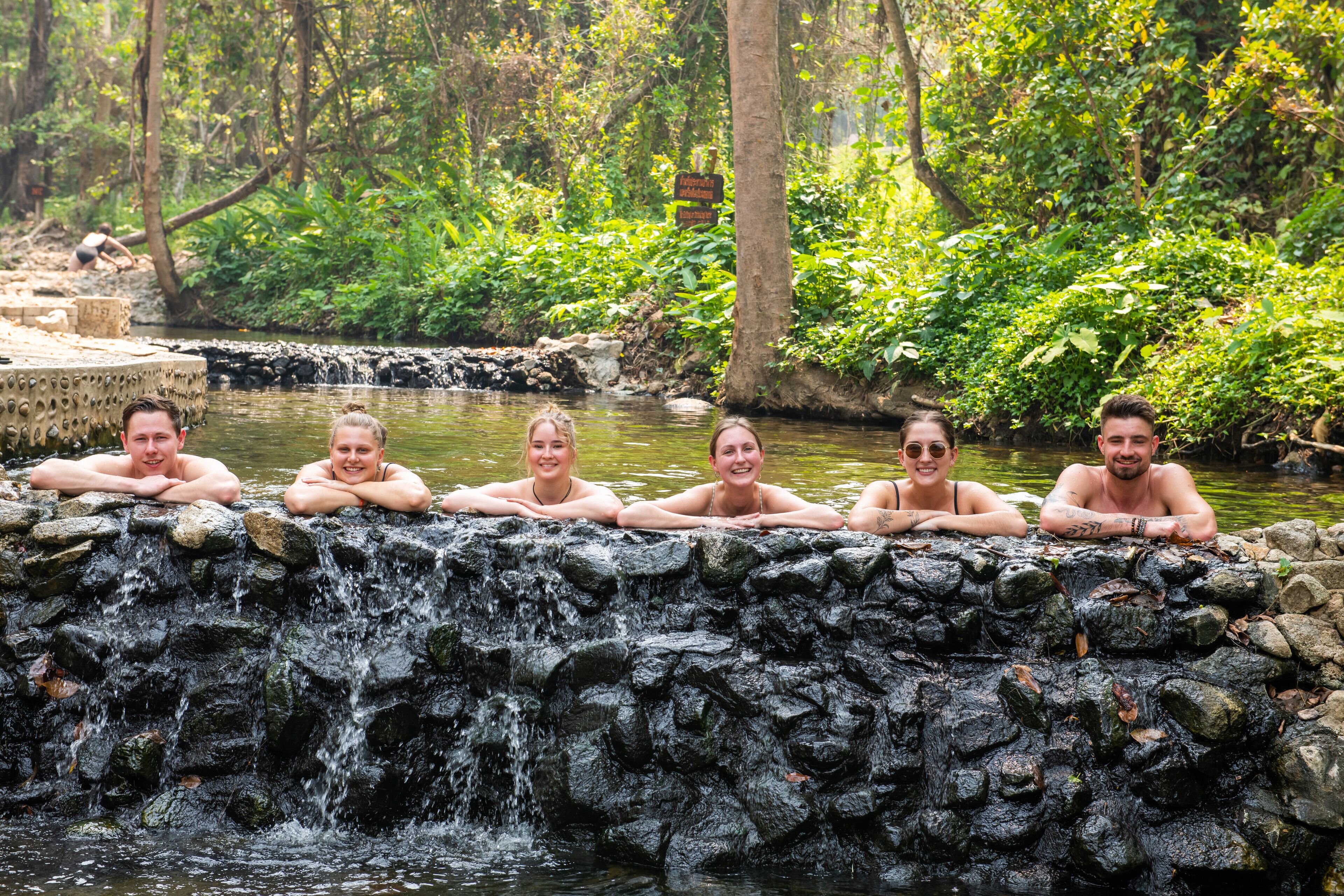 A group of people relaxing by a natural water feature surrounded by greenery.