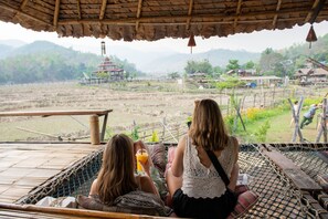 Two people relaxing on a hammock with a view of a rural landscape and traditional buildings. - Mad Monkey Pai (Pai)