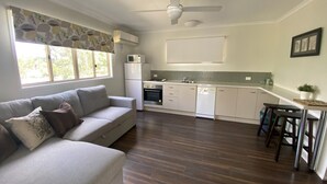 A modern kitchen with white cabinets, a built-in oven, and a microwave. There is a grey sofa with cushions in the living area. - Fairview at Imbil Country Cabins (Imbil)