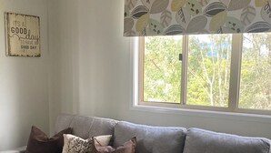 A grey sectional sofa with a window above it, a decorative leaf-patterned valance, and a 'It's a good day to have a good day' sign on the wall. - Fairview at Imbil Country Cabins (Imbil)