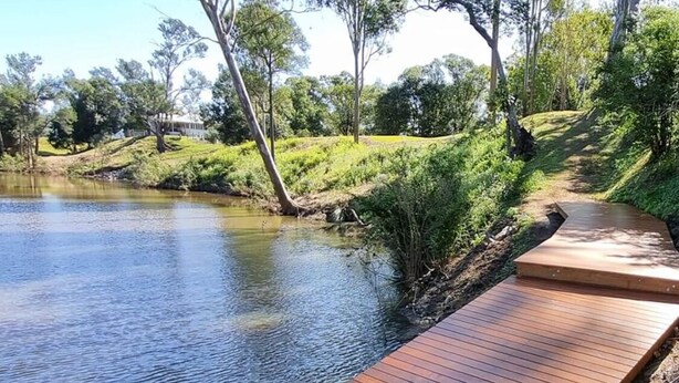 A wooden boardwalk extending over a rocky shoreline beside a calm body of water, surrounded by lush greenery and trees. - Fairview at Imbil Country Cabins (Imbil)