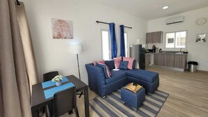 Un salon moderne avec un canapé bleu, une table à manger avec des chaises, et une cuisine en arrière-plan.