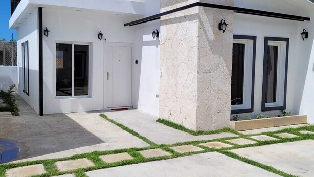 Une maison moderne à l’extérieur blanc, avec un mur d’accent en pierre et une terrasse pavée agrémentée de motifs d’herbe.