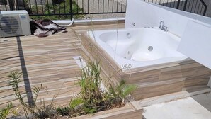 Une terrasse sur le toit avec un jacuzzi, une plateforme en bois et un jardinier avec des plantes.