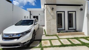 Une maison moderne à l’extérieur blanc, avec une allée et une voiture blanche garée.