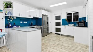 Een moderne keuken met witte kasten, een centraal eiland, een roestvrijstalen koelkast, een magnetron en een blauwe spatwand.