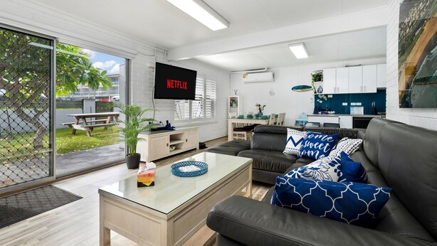 A modern living room with a sofa, coffee table, and a TV displaying 'NETFLIX'. - SKYES BEACH HOUSE | spas | sauna | arcade machines (Malua Bay)