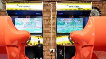Twee race spelautomaten met schermen waarop racegames worden getoond, een dartbord, en een persoon die ertussen staat.