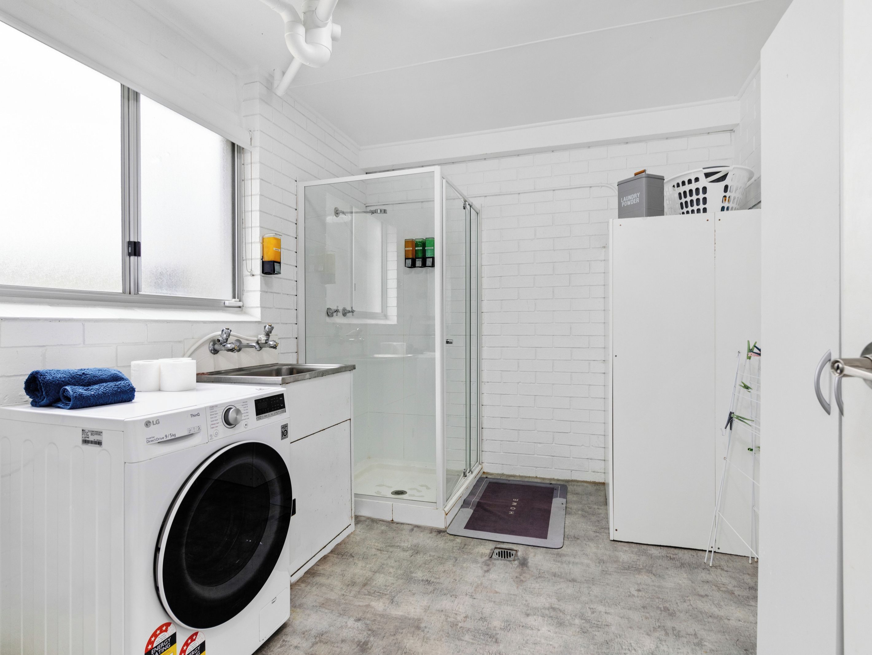 A laundry room with a washing machine, a sink, and a glass-enclosed shower.