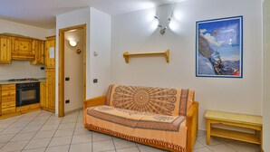 Una sala de estar con un sofá, un banco de madera, una cocina con armarios de madera, una estufa y un cuadro en la pared.