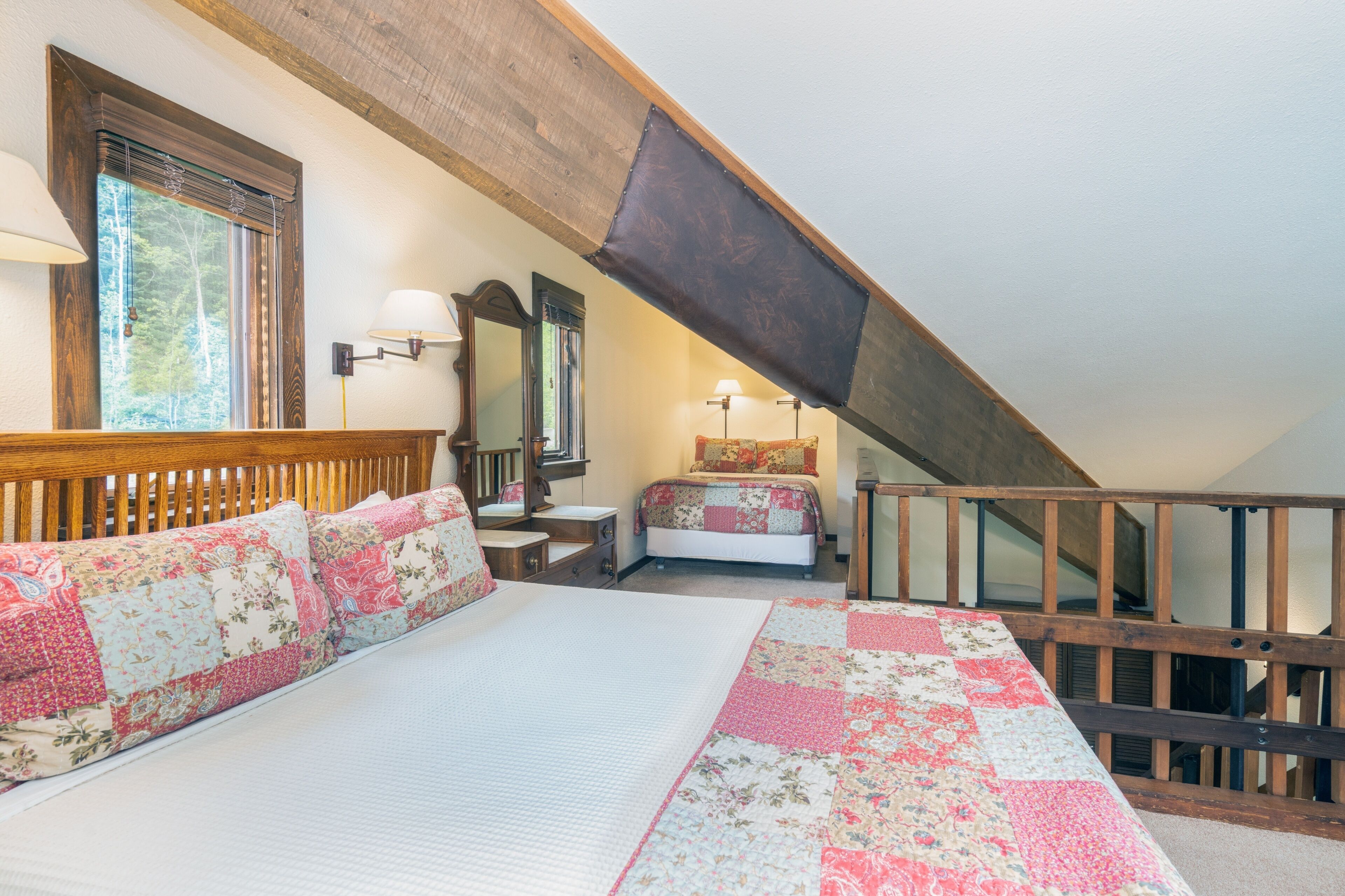 Ein Schlafzimmer mit einem hölzernen Kopfteil, einem Bett mit floralem Bettzeug, einem Nachttisch, einem Schminktisch und einem Fenster mit Jalousien.