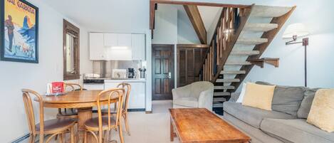 A dining area with a wooden table and chairs, a sofa, and a staircase.