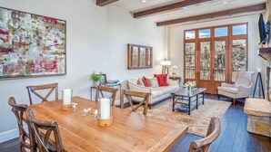 A spacious living room with a wooden dining table, a sofa, and a large window with a view of trees.