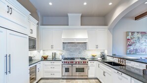 A modern kitchen with white cabinetry, a stainless steel Wolf oven, and a black sink with copper faucets.