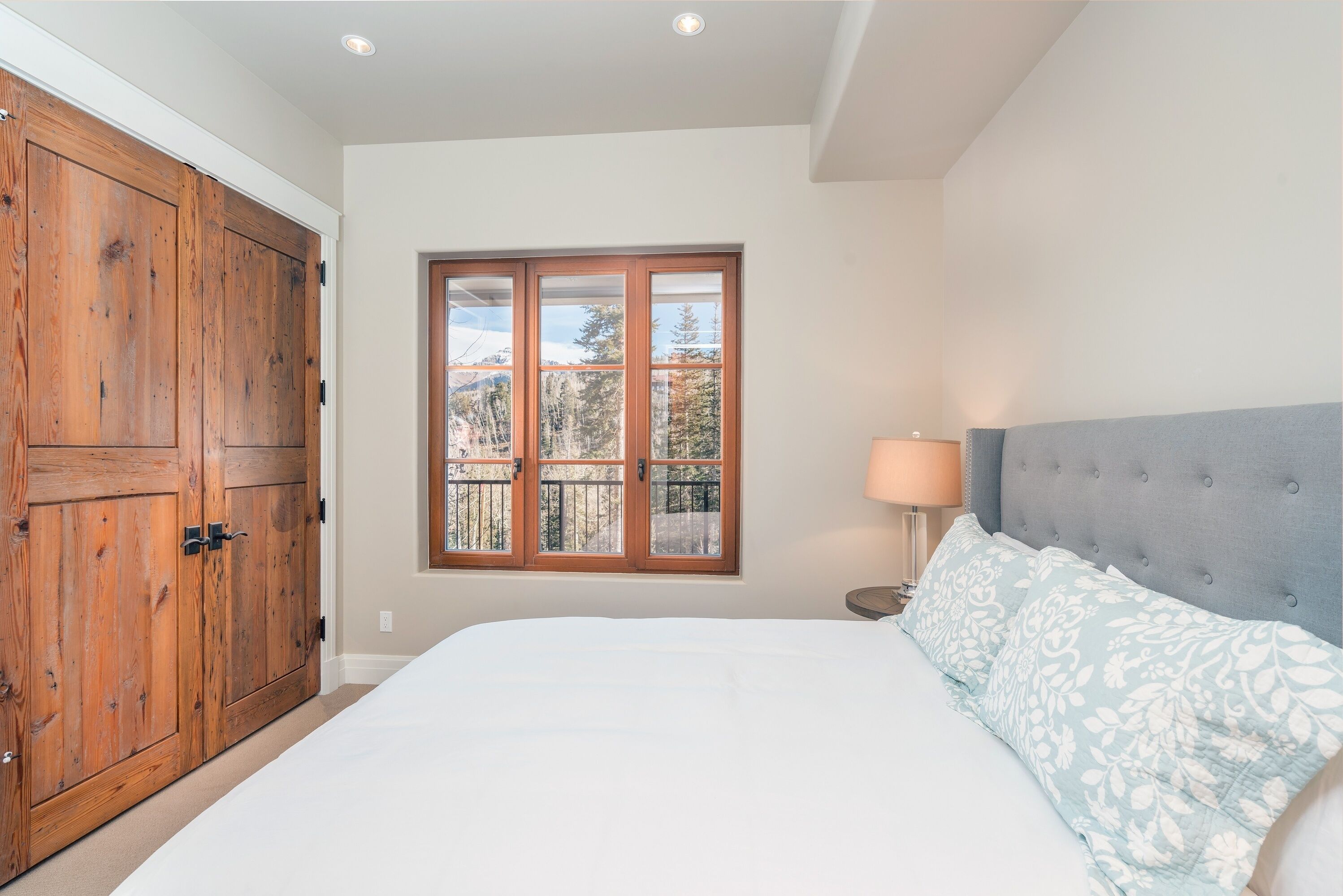 Un dormitorio con una cama grande, una ventana con vista a árboles y un armario de madera.