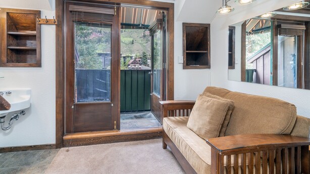 Una habitación con un banco de madera, un lavamanos, una puerta que da al exterior y un espejo en la pared.