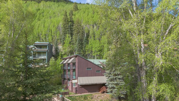 A multi-story building with a wooden deck and a small pond, surrounded by dense forest. - Manitou Lodge 11 Hotel Room by Alpine Lodging Telluride (Telluride)