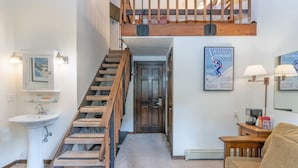 En trappa som leder upp till ett loft, ett handfat, en soffa och en inramad affisch på väggen.