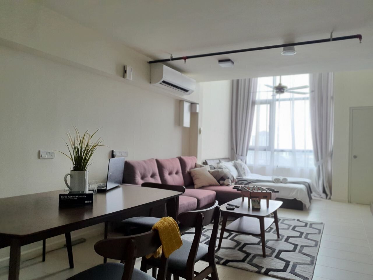 A modern living room with a sofa, a dining table, and a coffee table. There is a plant on the table, and a window with curtains.