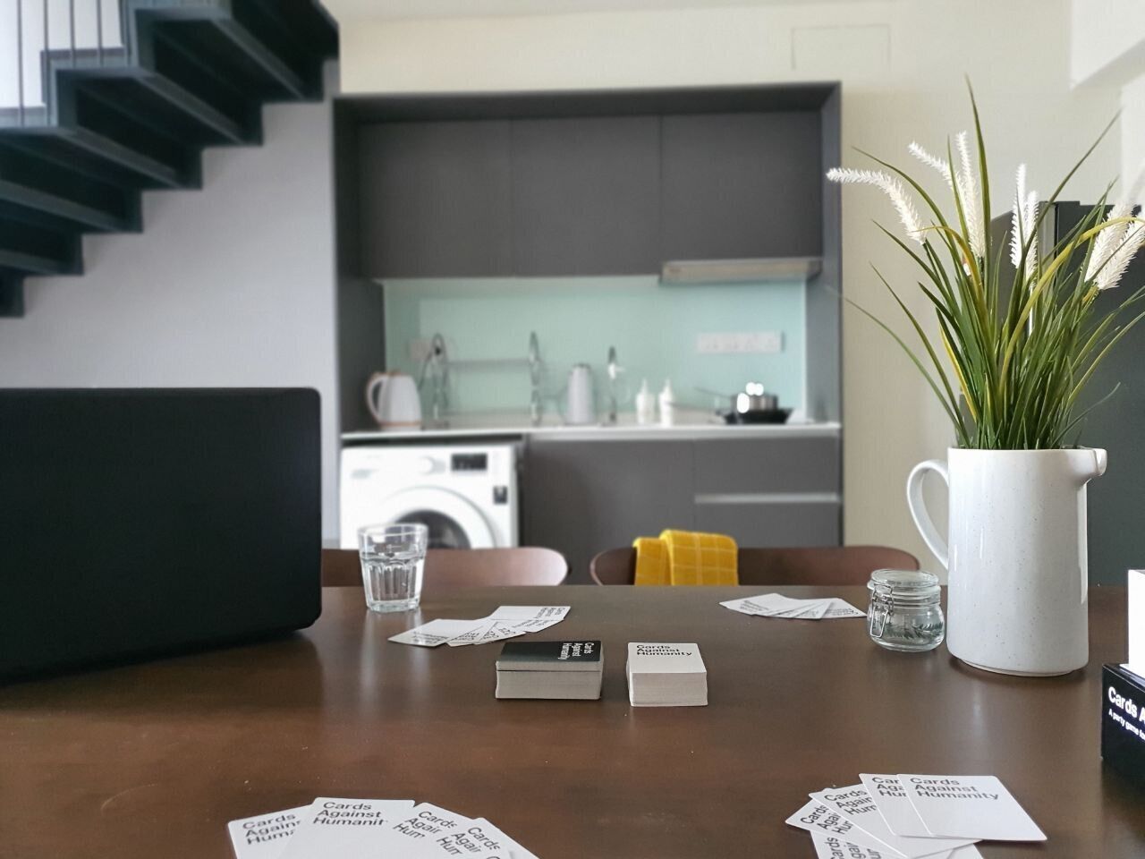 A dining area with a table set for two, a white pitcher, and a small plant.