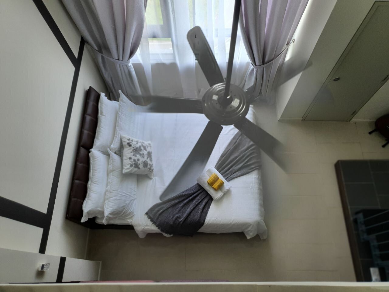 Een bed met een plafondventilator, witte beddengoed en een klein, geel object op het bed.