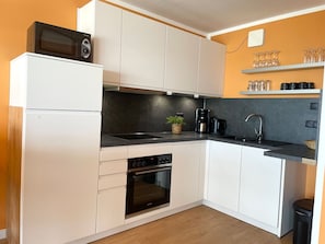 Una cucina compatta con mobili bianchi, un piano di lavoro nero, forno integrato, macchina da caffè e microonde.