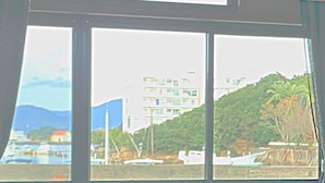 A view through a window with a building, trees, and boats. - Alloggio Nanki Shirahama (Shirahama)